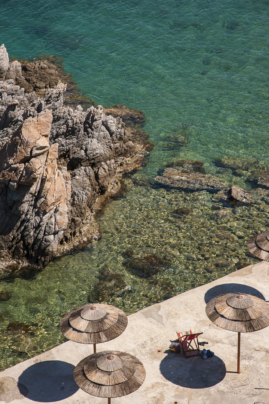 Felsige Badebucht mit klarem Wasser und Sonnenschirmen auf Sizilien